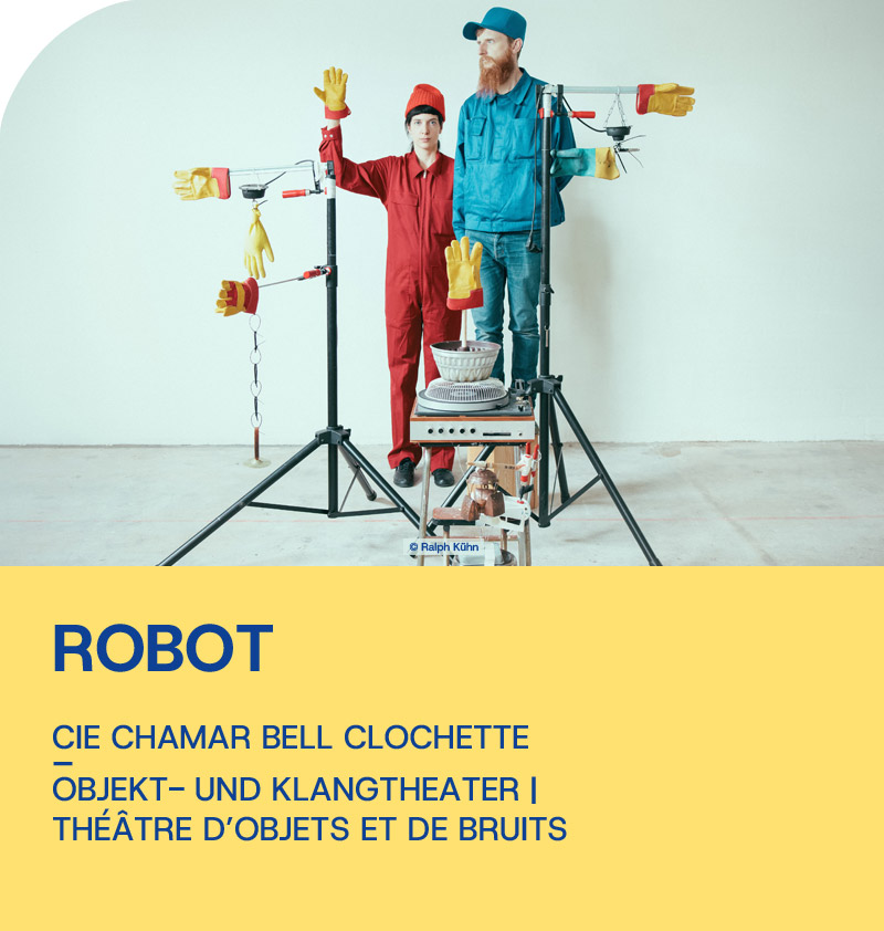 Robot - Szenenbild Eine Frau und ein Mann stehen hinter einer kleinen Maschine. Auf Ständern sind Handschuhe montiert, die in unterschiedliche Richtungen weisen.